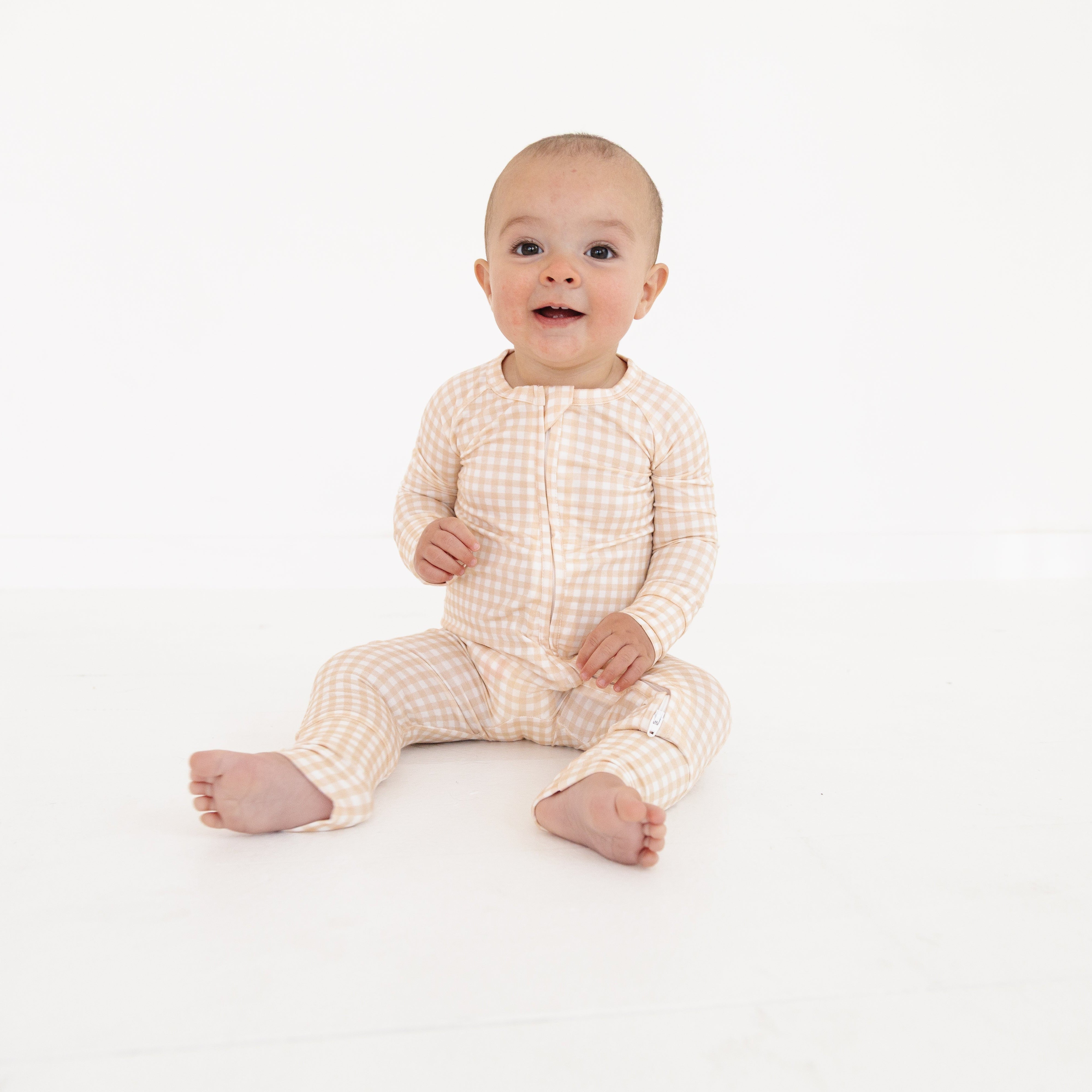Newborn in bamboo zipper romper with beige check print, highlighting fold-over cuffs and two-way zipper.