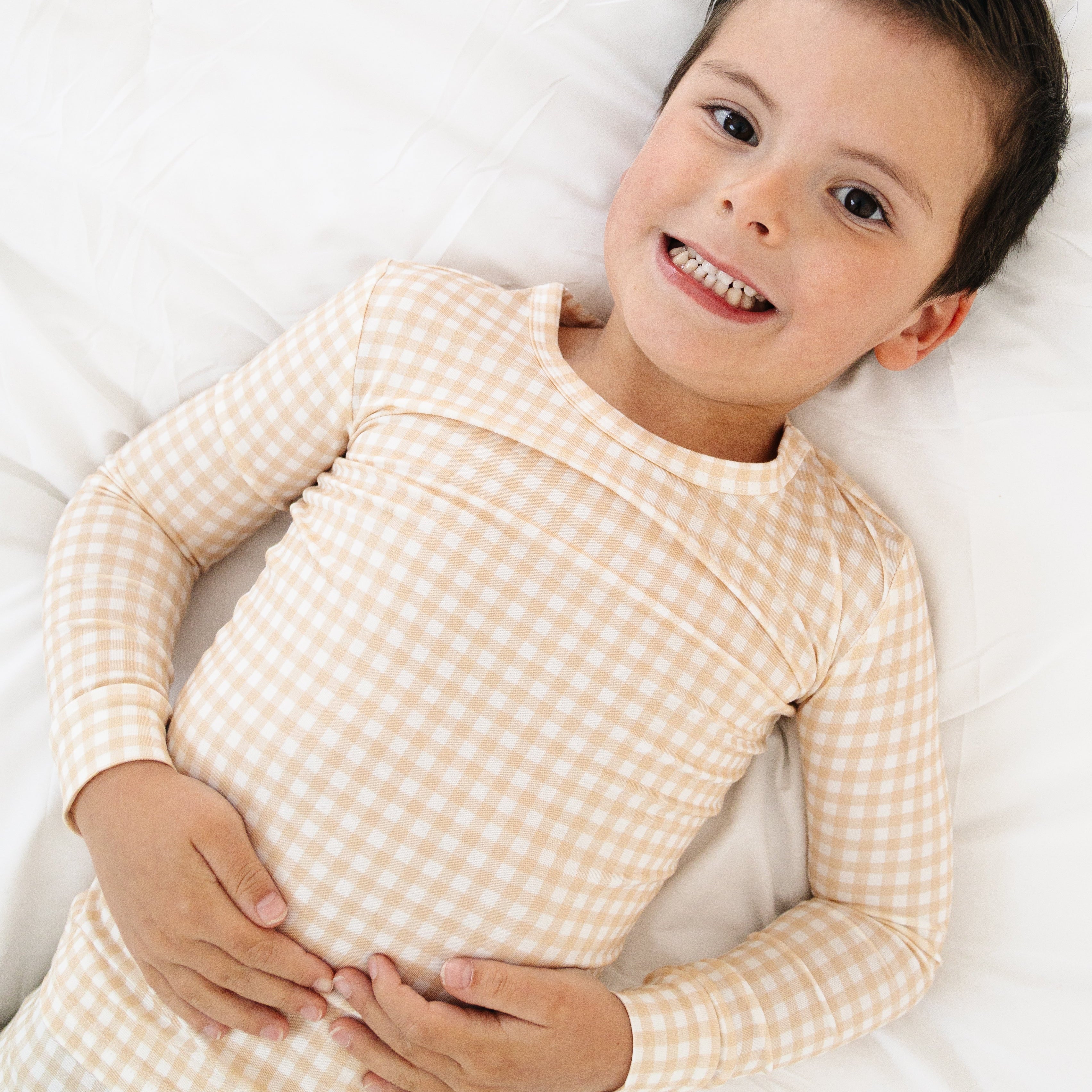 Toddler boy lying down in beige check pajama set, relaxed and cozy on a soft surface.