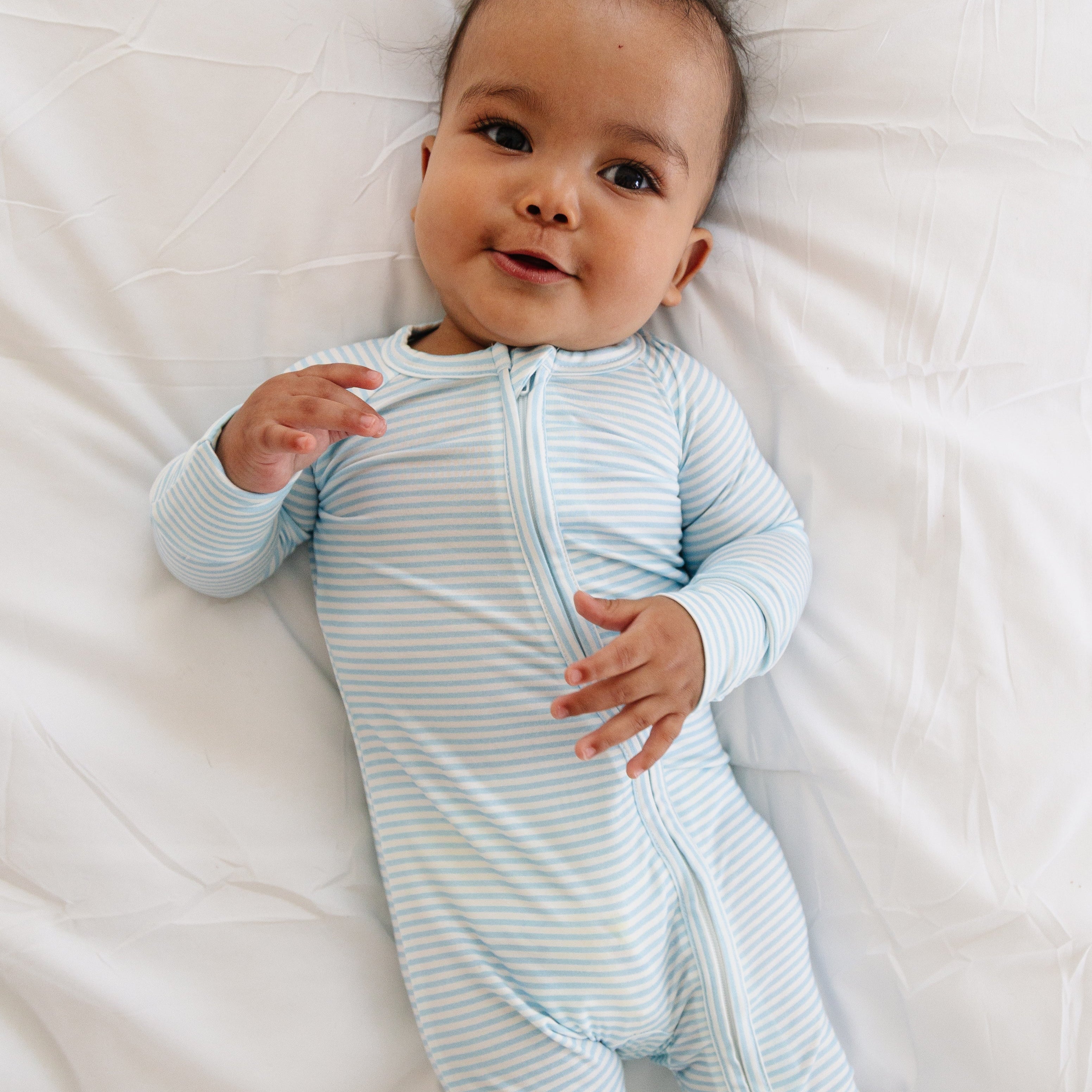 Baby boy laying on his back in the Seaside Stripe sleeper, looking up with a relaxed expression.
