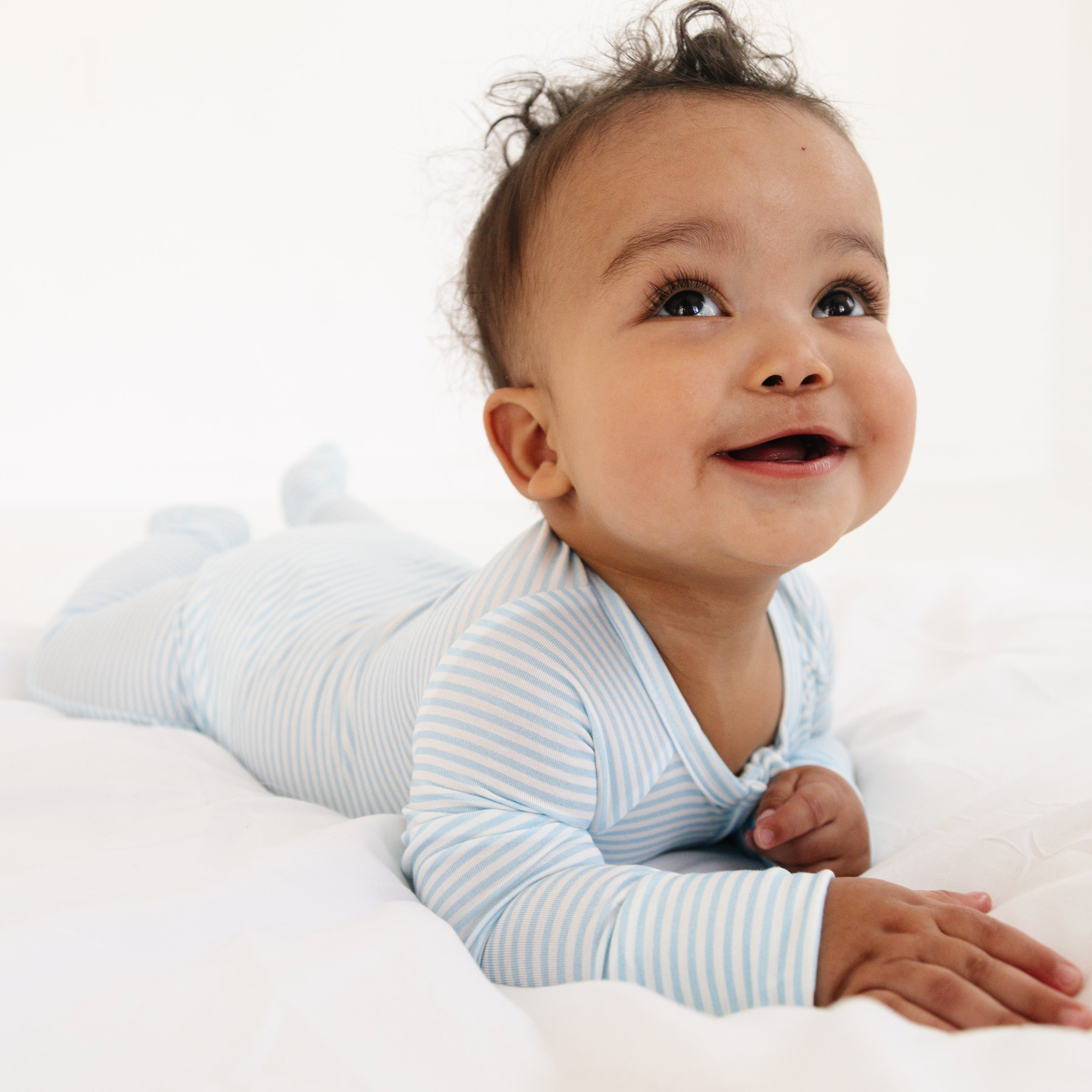Baby boy laying on his tummy, wearing the Seaside Stripe sleeper, showing the back view and soft bamboo fabric.