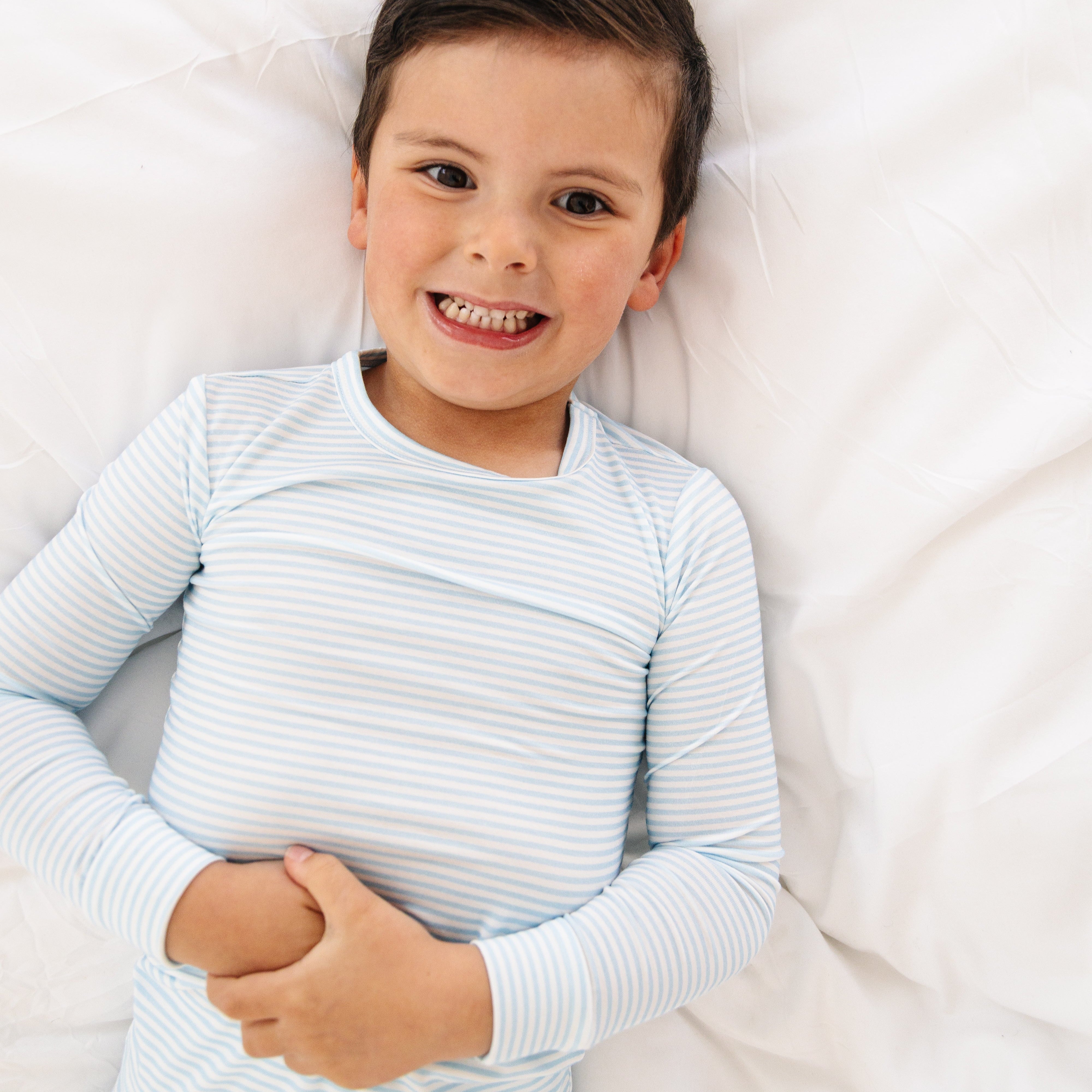 Toddler boy laying flat on his back in the Seaside Stripe pajamas, arms stretched out, showing the comfortable fit.