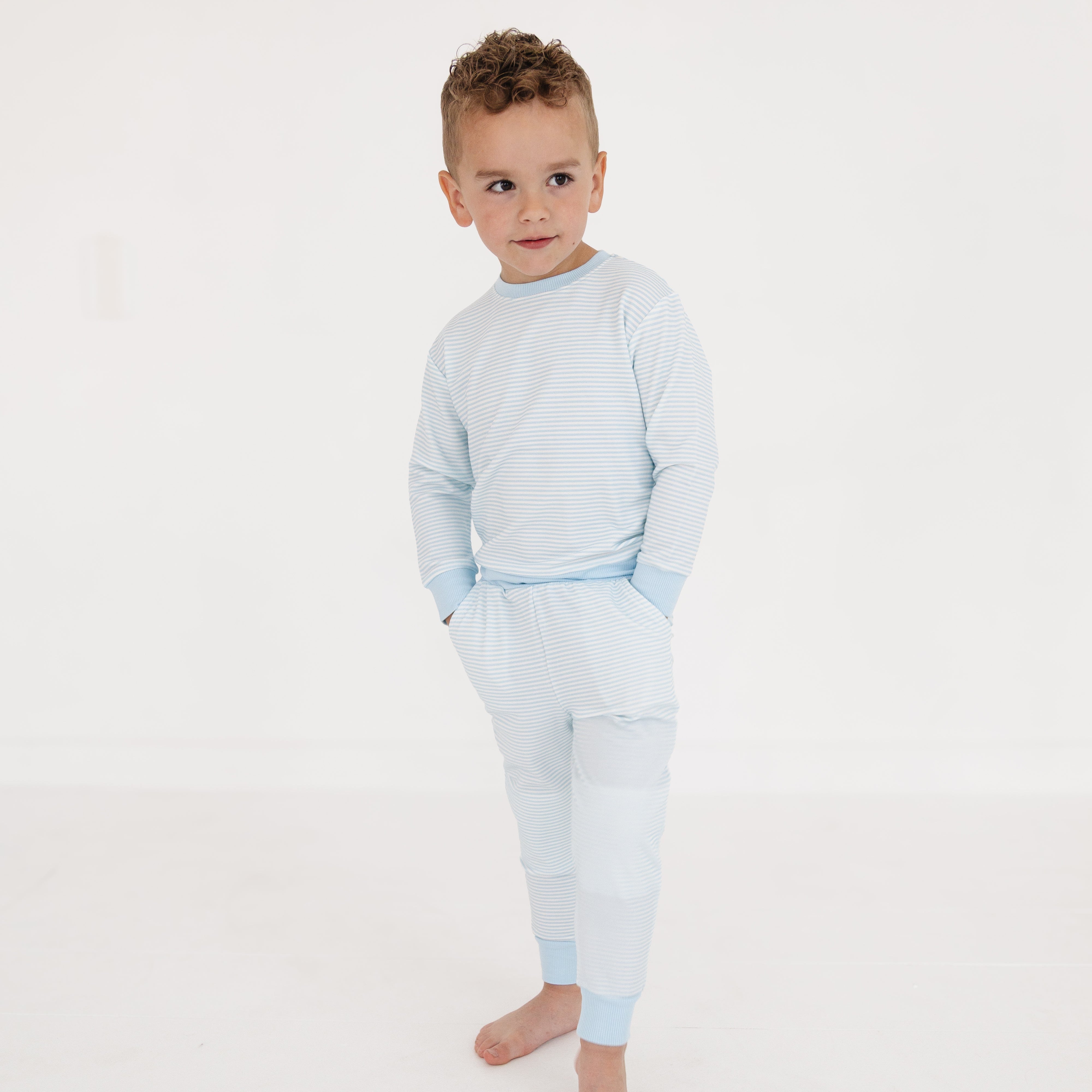 Boy standing with hands in his pockets wearing Motette’s striped blue bamboo lounger sweatsuit, smiling confidently