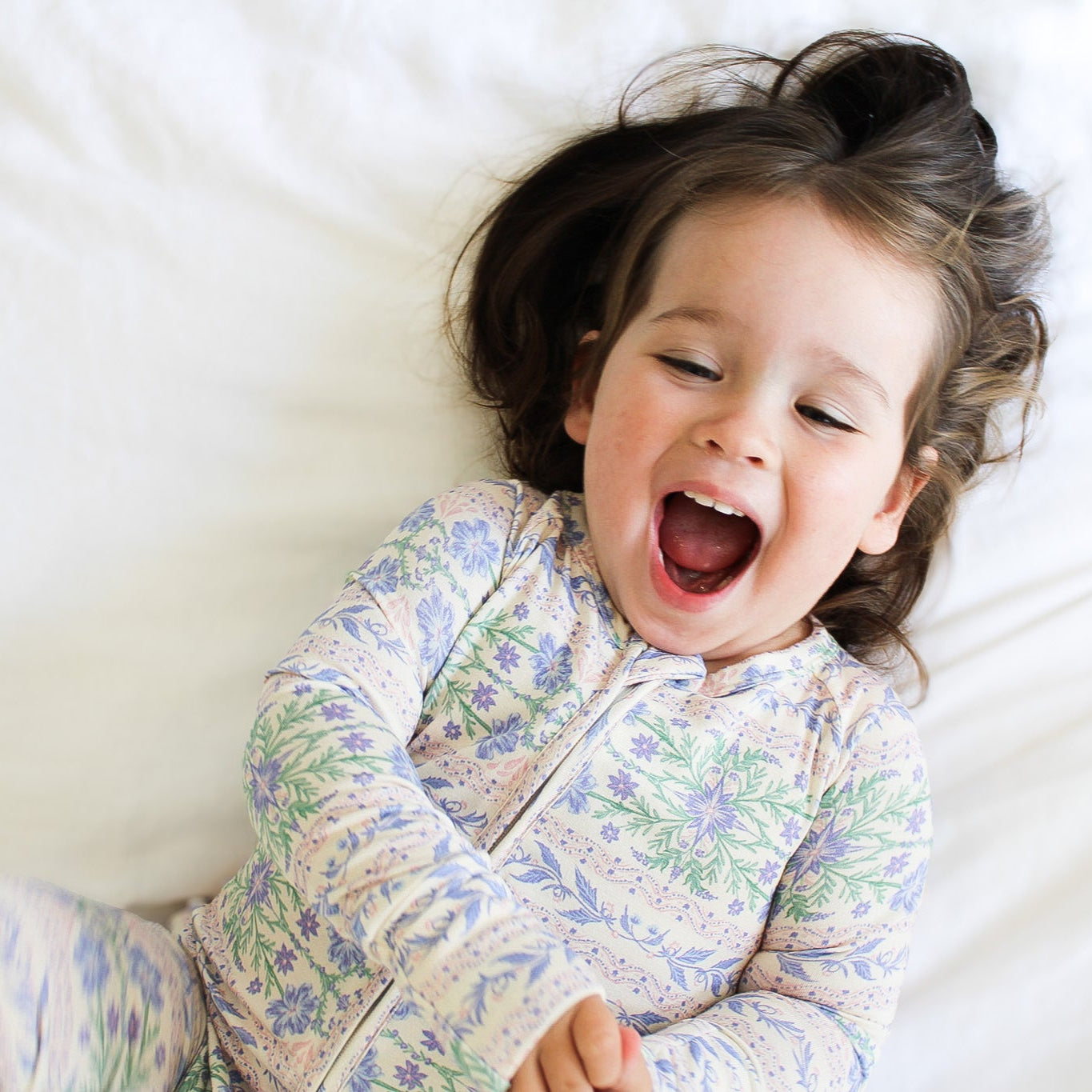 Baby laying down in Motette’s pink and purple floral bamboo zipper romper sleeper, resting on a soft white blanket