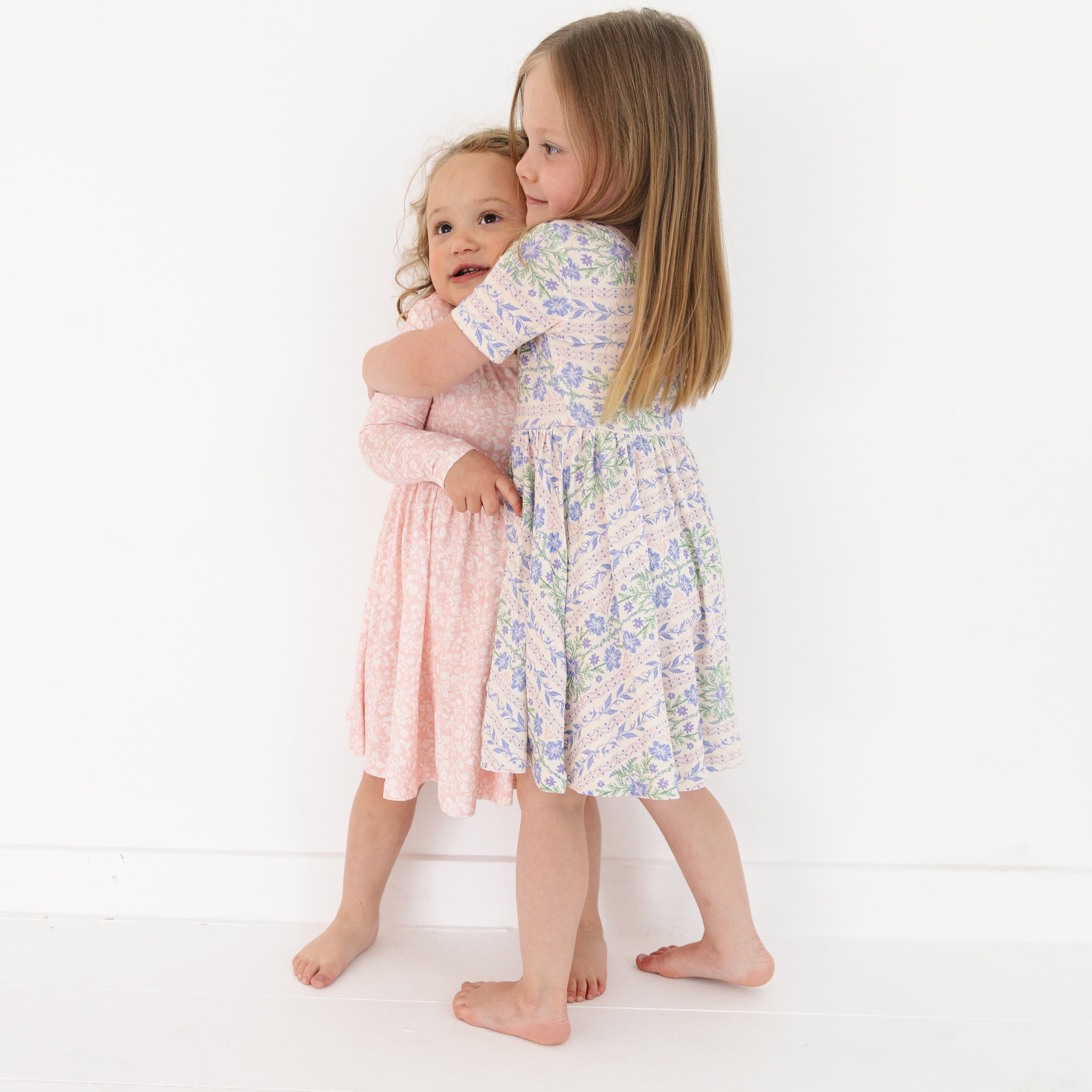 Two sisters wearing Motette twirl dresses—one in short sleeves, the other in long sleeves—laughing together
