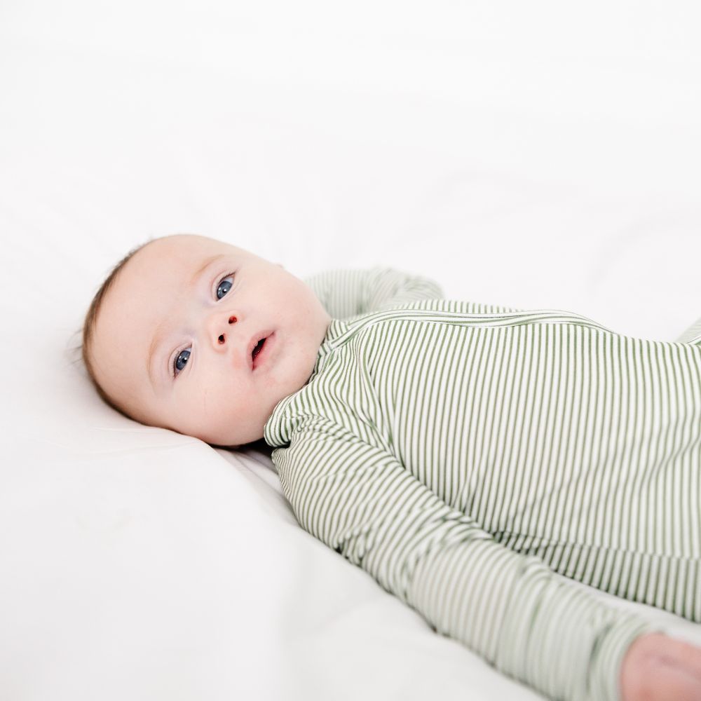 Baby lying on bed wearing Motette Evergreen Stripe Bamboo Sleeper, soft bamboo pajamas.