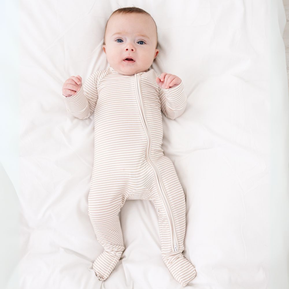 Baby lying on bed wearing Motette Oatmeal Stripe Bamboo Sleeper, soft striped pajamas.