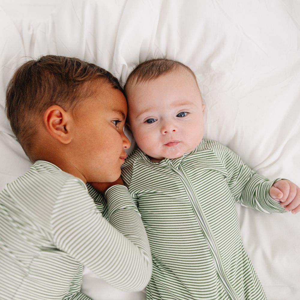 Baby cuddling with sibling in matching Motette Evergreen Stripe Bamboo Sleeper pajamas.