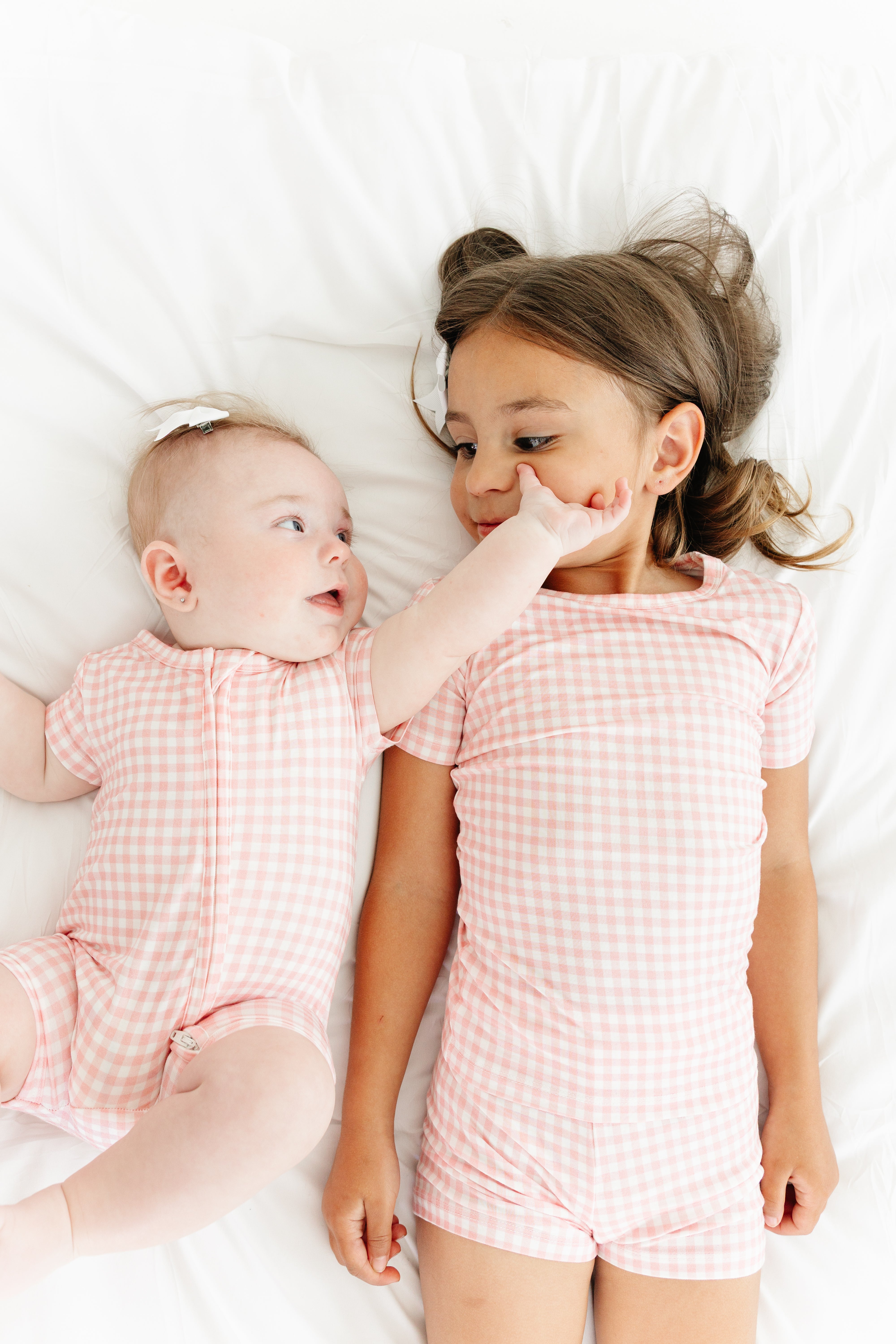 Baby and sister lying down together wearing Sugar Gingham bamboo sleepers by Motette