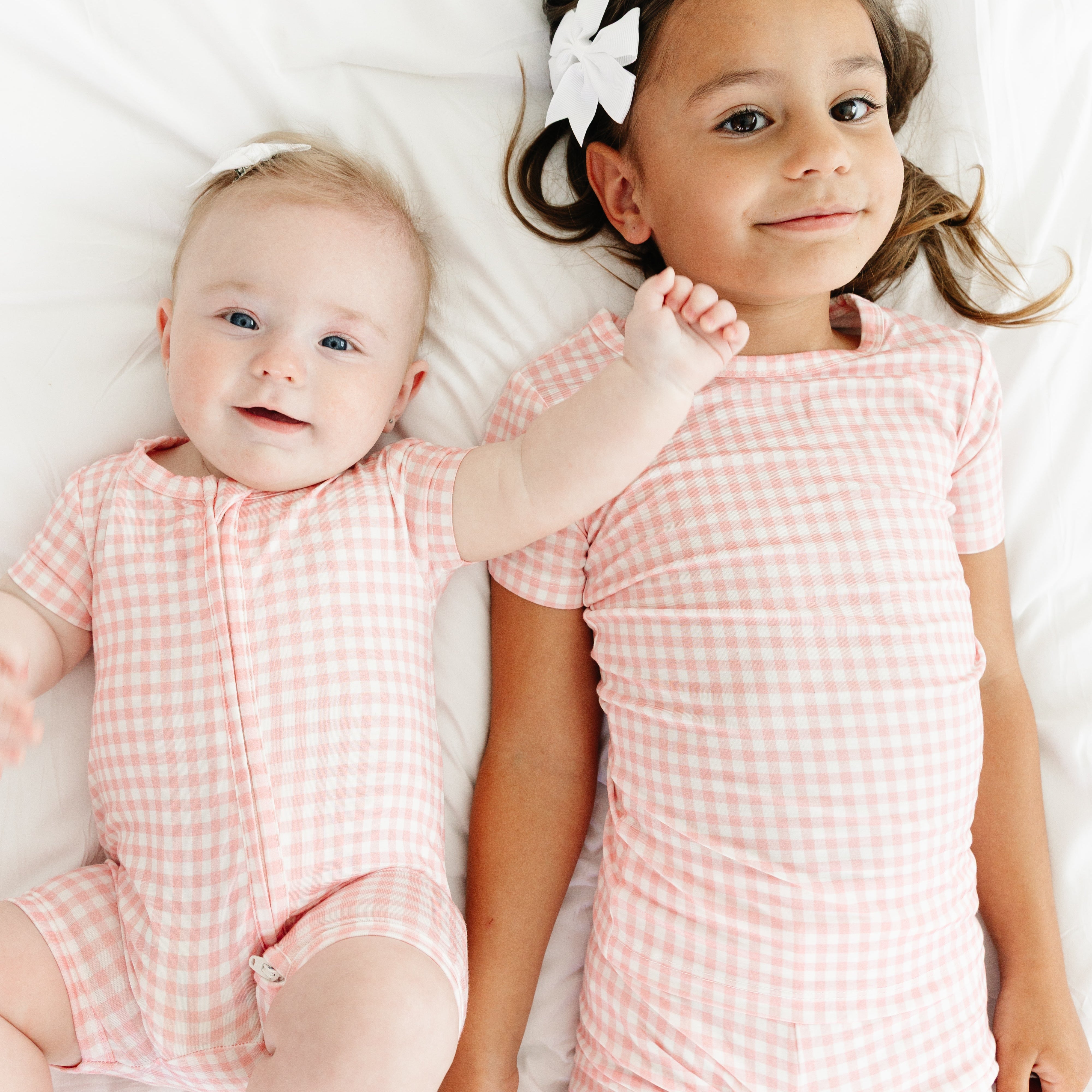 Baby smiling with her sister while both wear Sugar Gingham bamboo sleepers from Motette