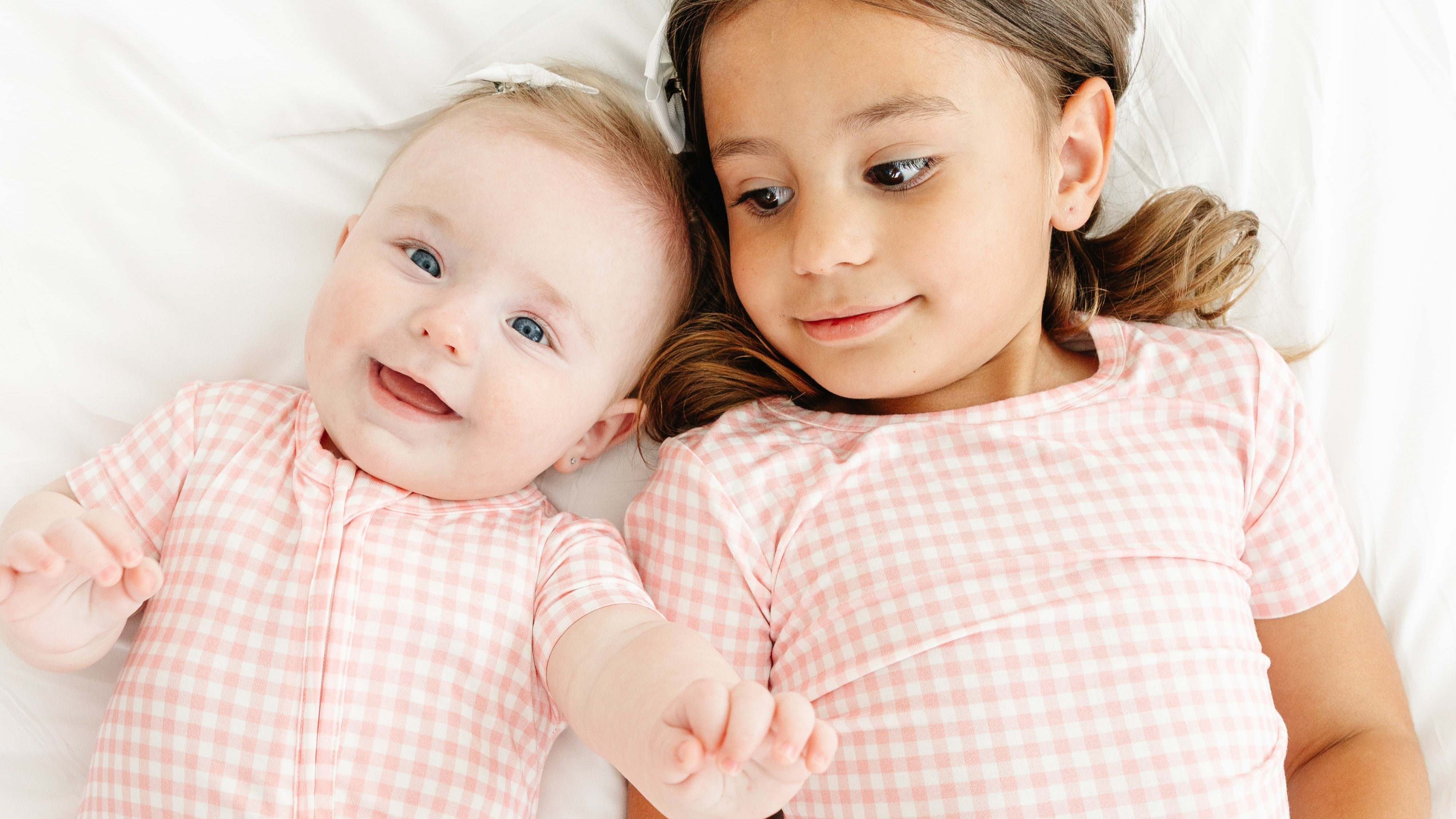 Baby girl smiling with her sister, both wearing Sugar Gingham bamboo sleepers from Motette