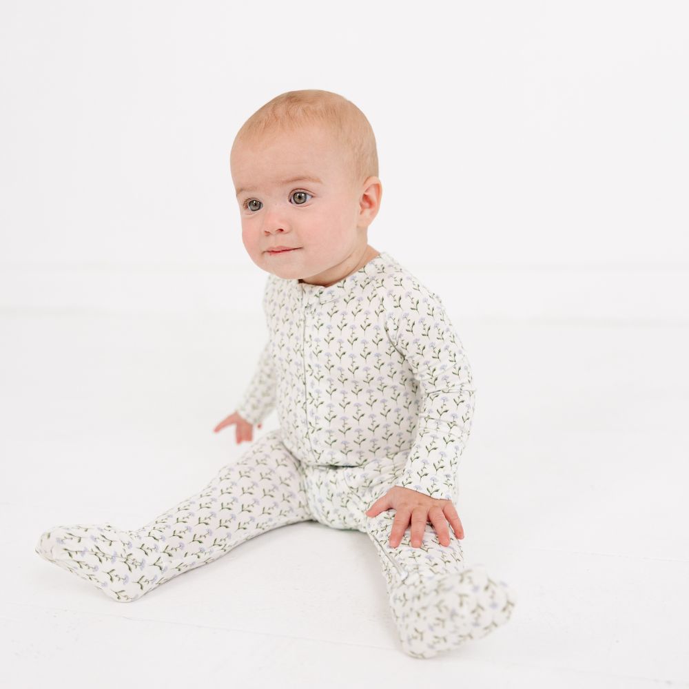 Baby sitting on the floor wearing Motette Lavender Lane Bamboo Sleeper, cozy and soft pajamas.