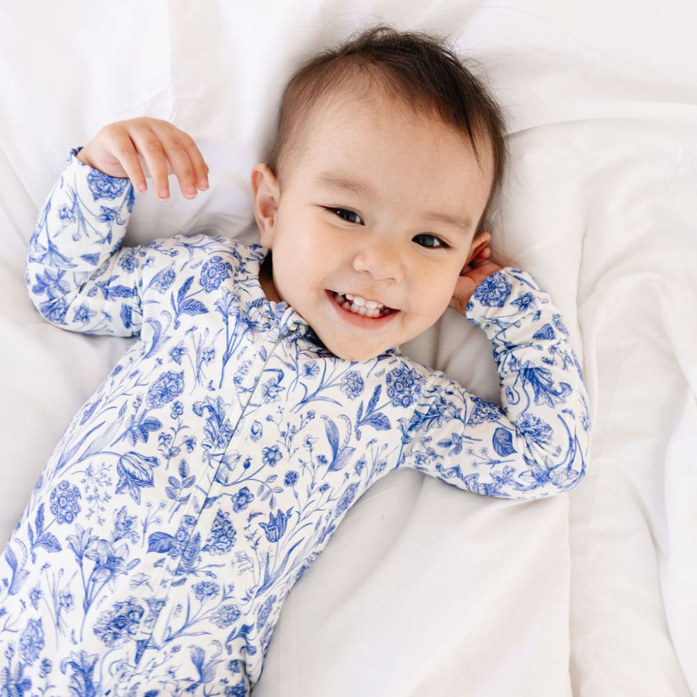 Baby smiling while lying on bed in Porcelain Vine bamboo zipper pajamas by Motette – soft, eczema friendly sleepwear for babies