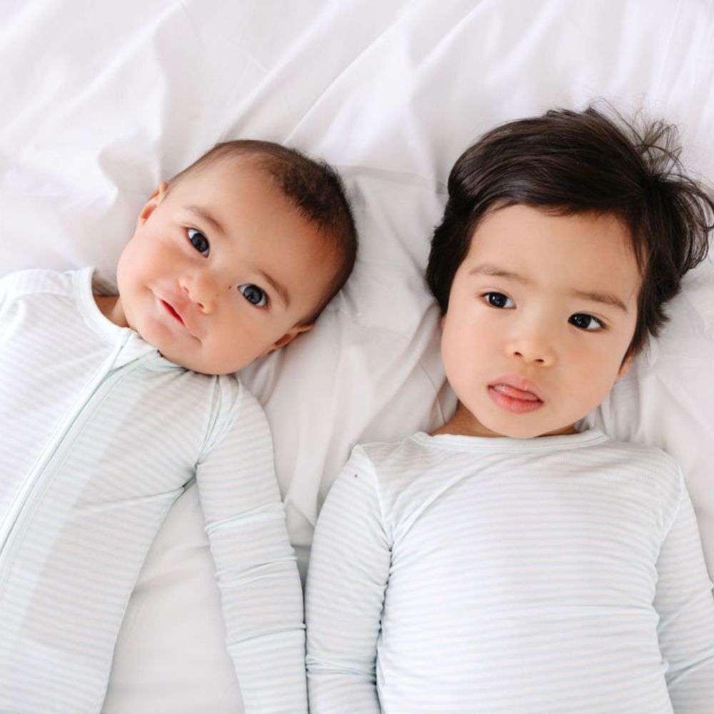 Baby and toddler lying side-by-side in Cloud Stripe bamboo sleepers by Motette – eczema friendly coordinated sibling sets