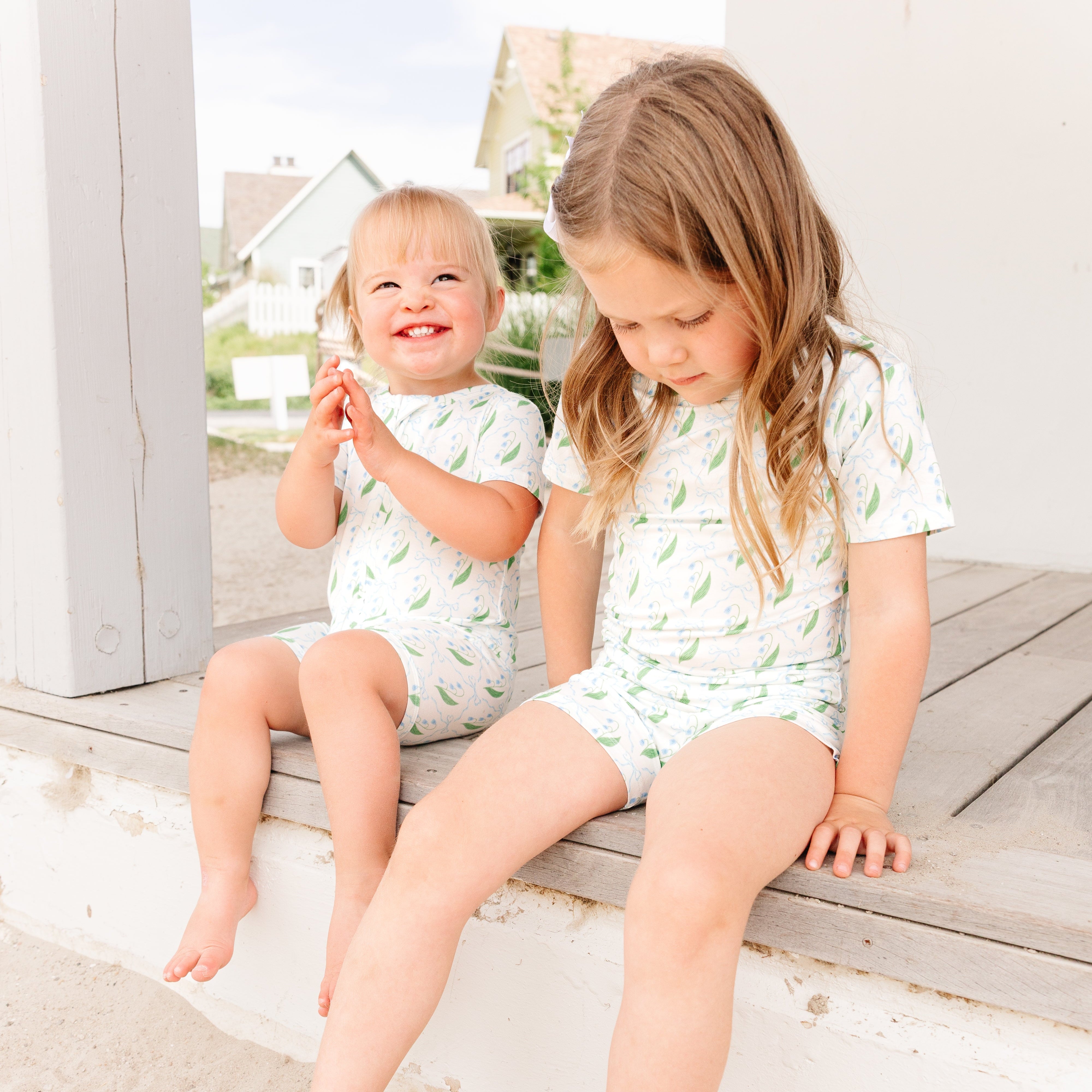Baby and toddler girl sitting outdoors wearing the Bluebell Bows bamboo pajama sets by Motette