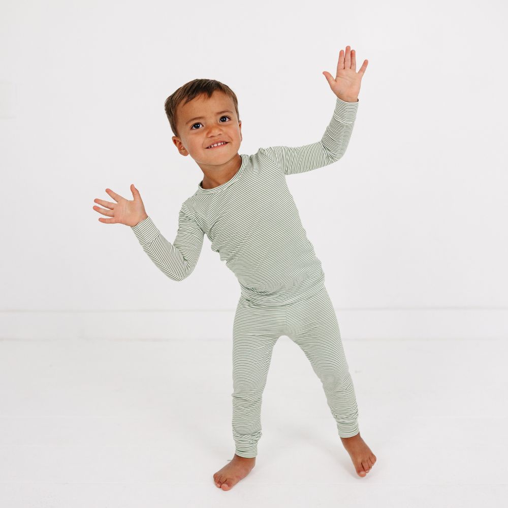 Little boy smiling and posing playfully in Motette Evergreen Stripe Bamboo Kids Pajama Set with green stripes.