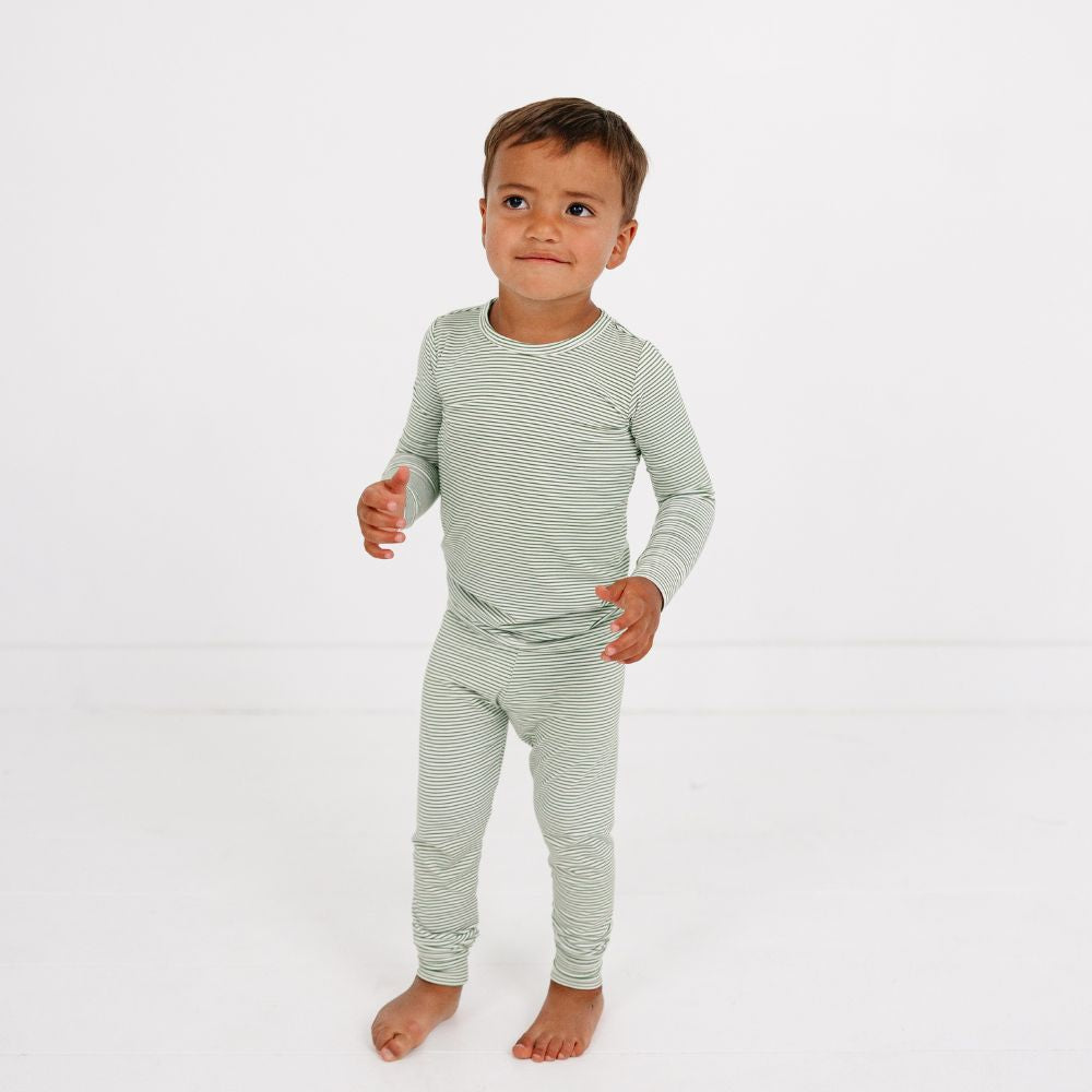 Little boy standing wearing Motette Evergreen Stripe Bamboo Kids Pajama Set with green stripes.