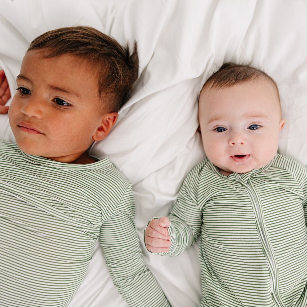 Two siblings lying side by side smiling in matching Motette Evergreen Stripe Bamboo Pajamas.