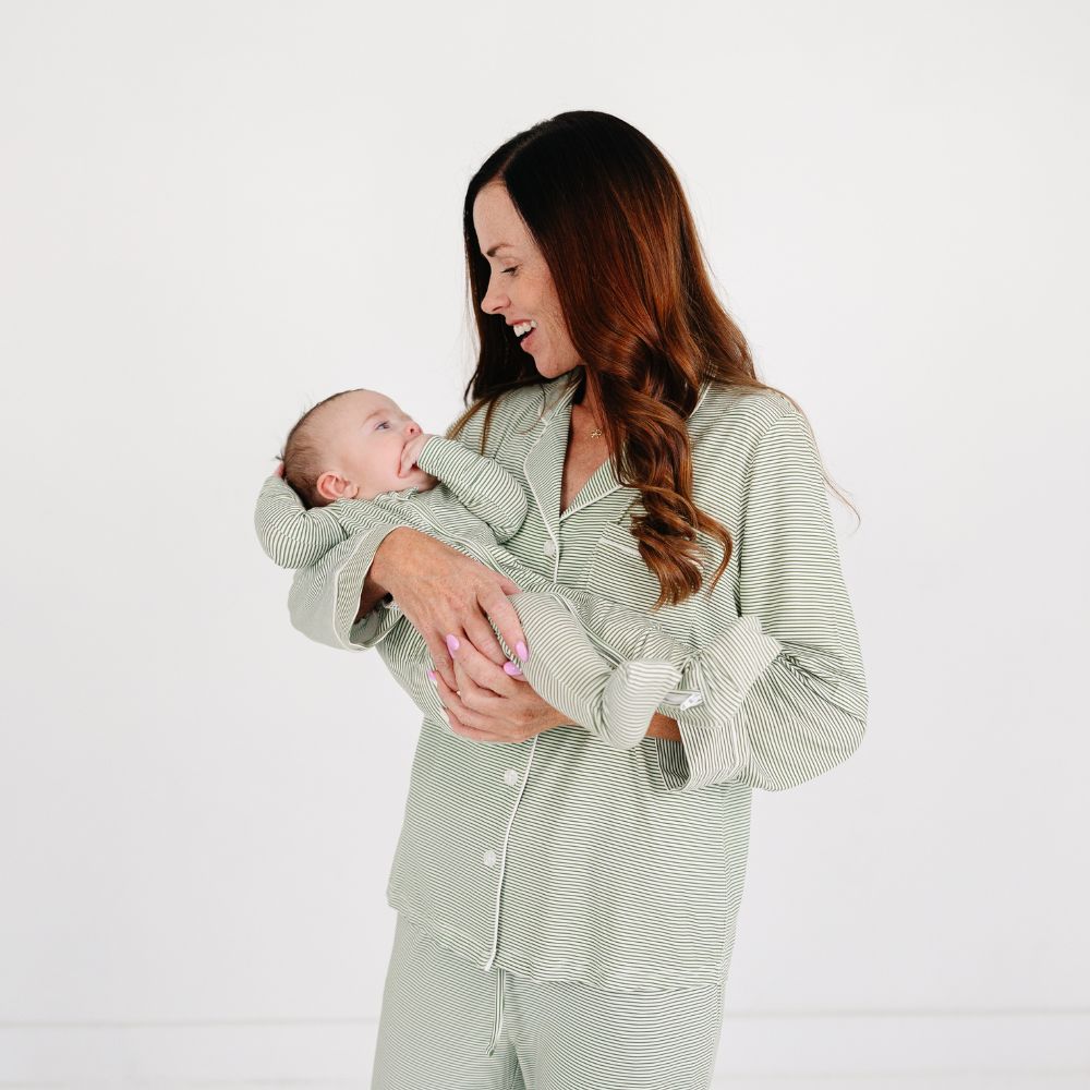 Mommy holding baby wearing matching Motette Evergreen Stripe Bamboo Pajama Sets, featuring a soft green and white striped pattern with button-up top and white piping details.