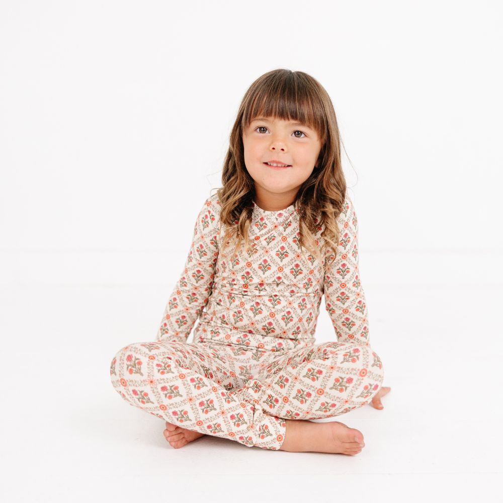 Young girl sitting cross-legged wearing Motette Holly Trellis Bamboo Kids Pajama Set, smiling at camera.