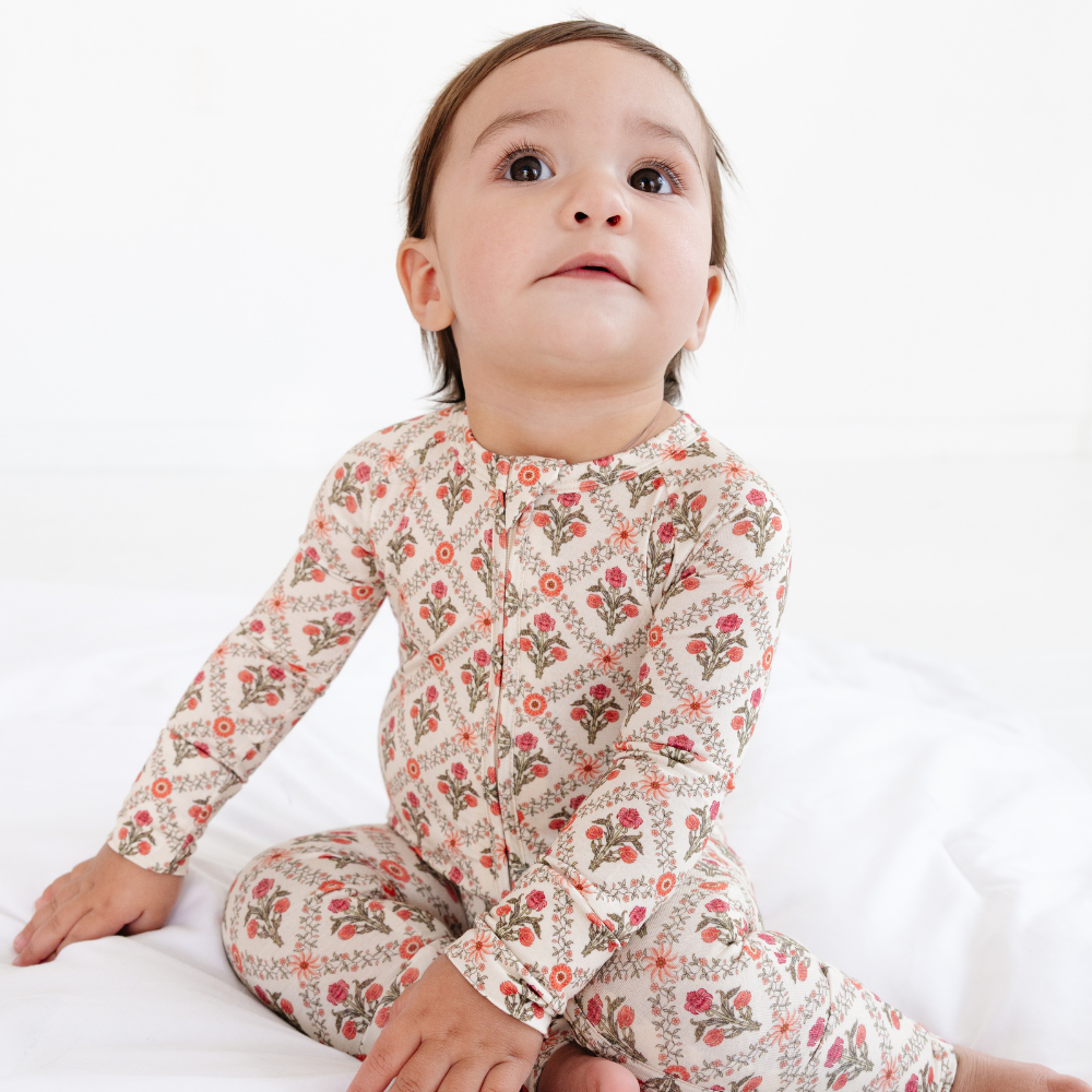 Close-up of a baby sitting and looking up wearing the Motette Holly Trellis Bamboo Sleeper, focusing on the detailed floral trellis print and the soft ribbed neckline.