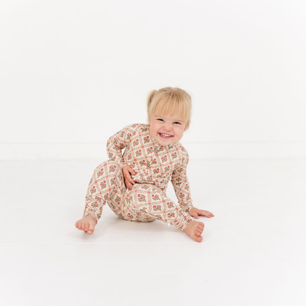 Baby sitting and smiling wearing Motette Holly Trellis Bamboo Sleeper with all-over floral print.