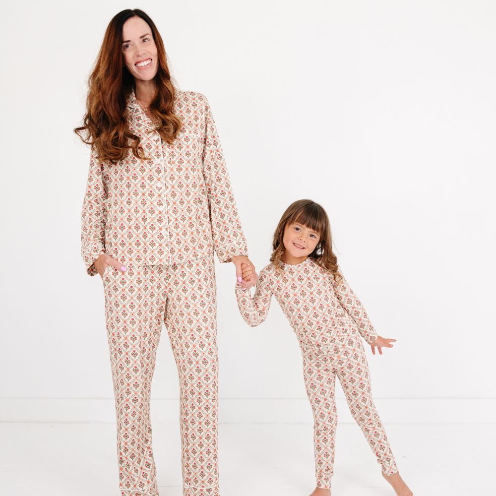Mommy and child wearing matching Motette Holly Trellis Bamboo Pajama Sets, featuring a cream background with red and green floral trellis print, with Mommy in a long-sleeve and pants set and child in a long-sleeve top and leggings.