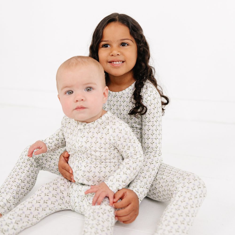 Older sister holding baby sibling while sitting, both wearing Motette Lavender Lane Bamboo Pajama Sets.