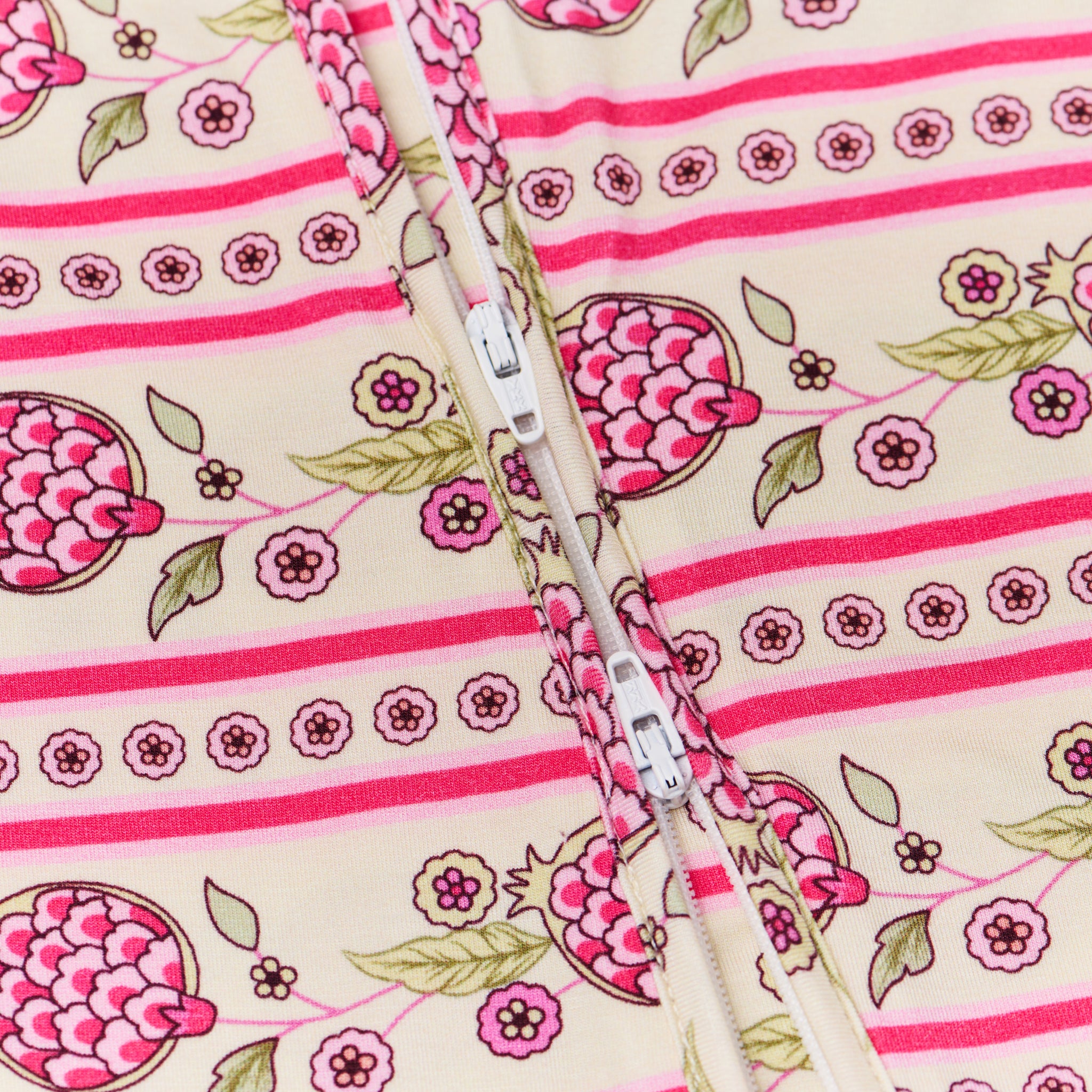 Close-up flatlay of the Motette Pomegranate Soiree Bamboo Sleeper, highlighting the functional double zipper for easy changes and the fold-over mitten and foot cuffs in a pink and white striped pattern.