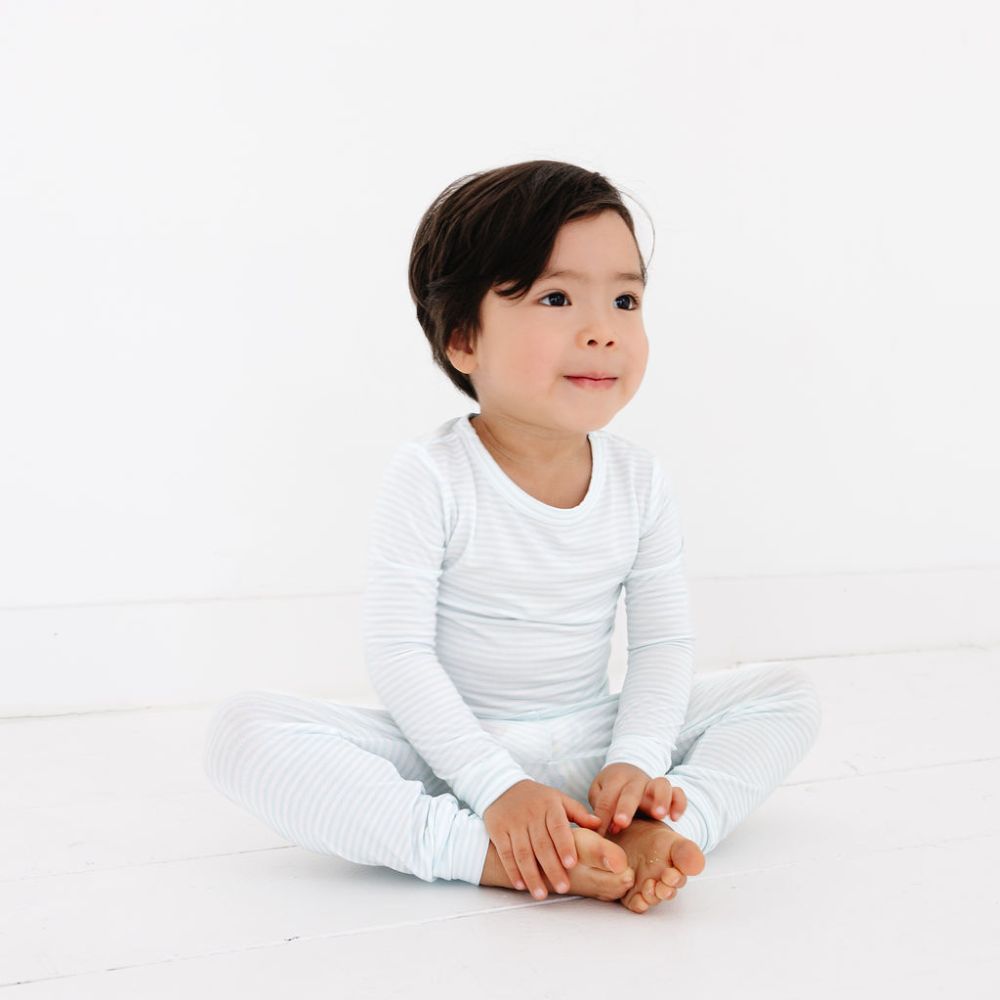 Toddler sitting cross-legged in Cloud Stripe bamboo pajamas by Motette – eczema friendly and breathable
