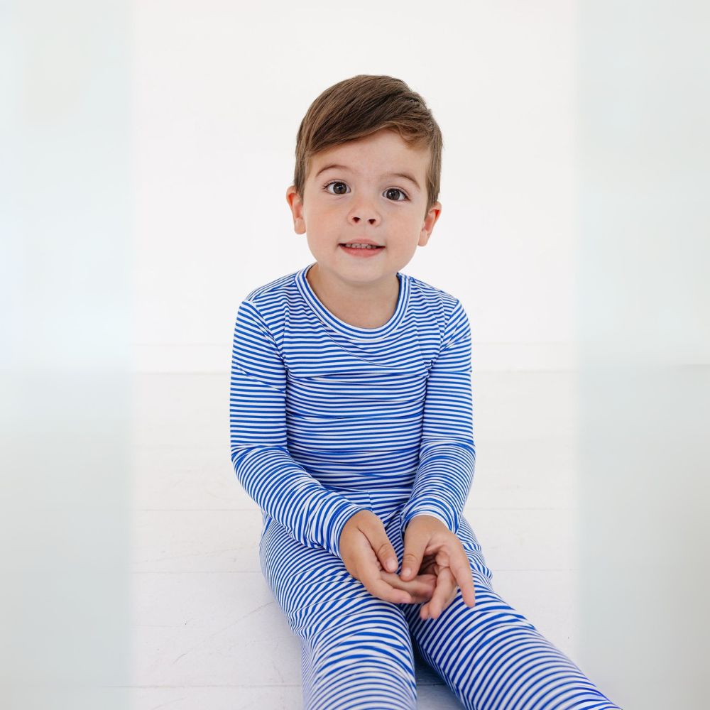 Toddler sitting on white floor in long sleeve bamboo pajama set in Cobalt Stripe by Motette – soft, eczema friendly sleepwear for kids