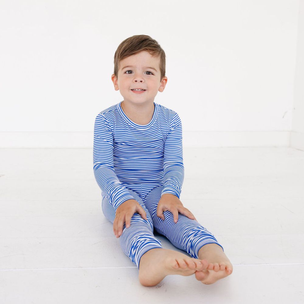 Toddler sitting with legs stretched out wearing Cobalt Stripe bamboo pajamas by Motette – soft and eczema friendly two-piece sleepwear set